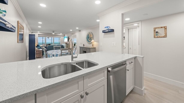 A modern kitchen with a double sink, stainless steel appliances, and a view to the living area. - Sanibel Surfside 115: Gorgeous Gulf Front Oasis! (Sanibel)