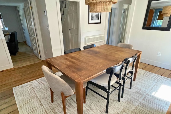 A dining area with a wooden table, six chairs, a woven light fixture, and a rug.