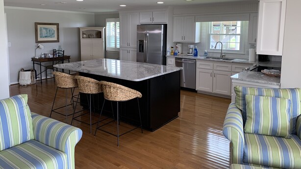 A modern kitchen with white cabinets, a stainless steel refrigerator, and a central island with bar stools.