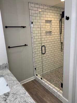 A walk-in shower with a glass door, tiled walls, and a granite countertop.