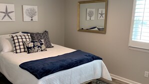 A bedroom with a bed, a ceiling fan, a large mirror, and artwork on the walls.