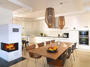 A modern kitchen with a central island, a dining area with a wooden table and chairs, and a built-in fireplace.