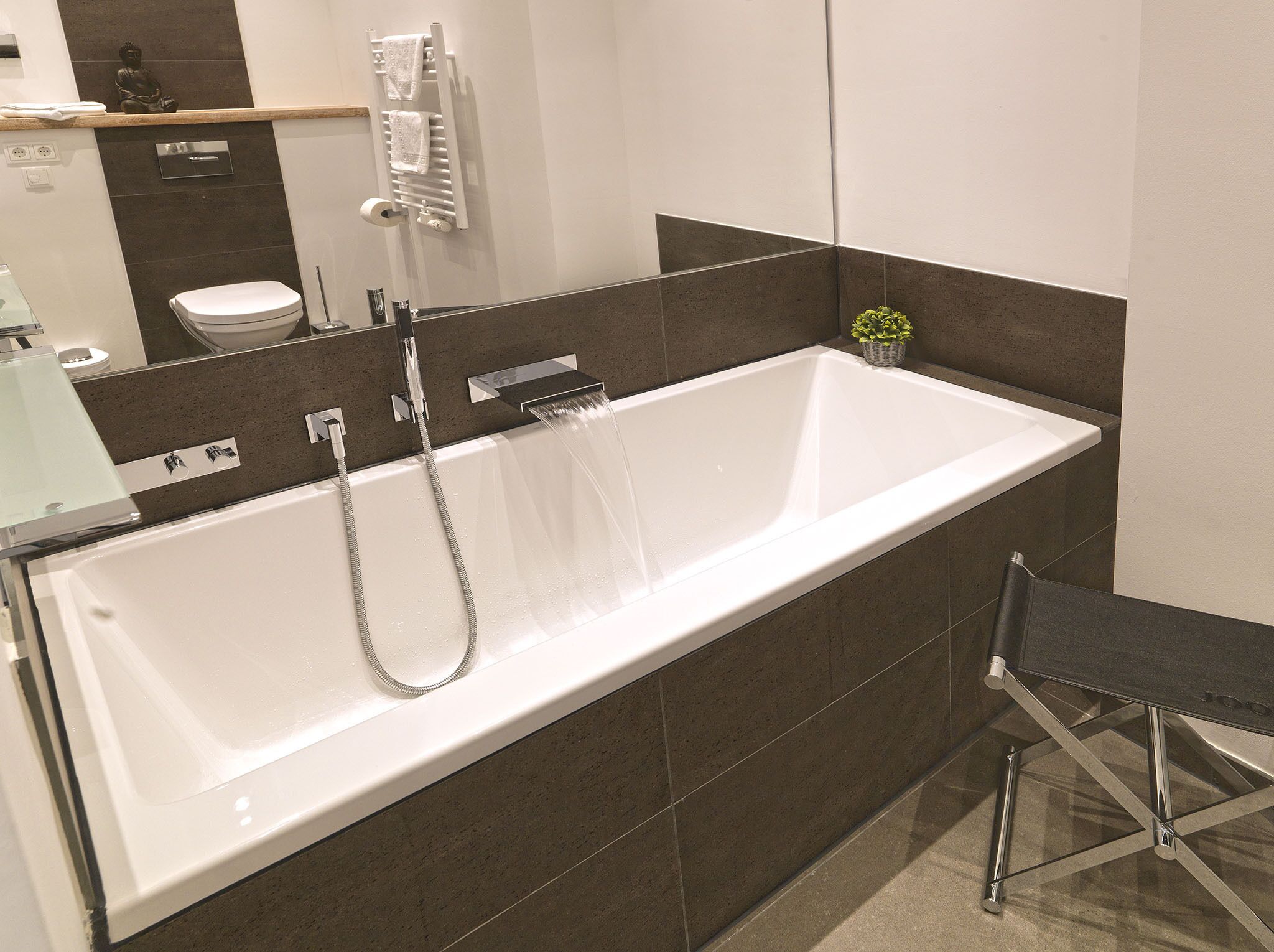 A modern bathroom with a large white bathtub, a handheld showerhead, and a toilet.
