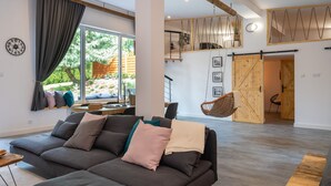 A modern living room with a large sofa, a hanging chair, and a wooden staircase leading to an upper level. - Secret Loft by Villa Jurka (Paszkówka)