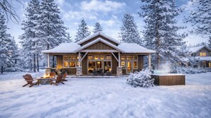 Eine schneebedeckte Lodge mit Kamin, Sitzgelegenheiten im Freien und einem Steinkamin.