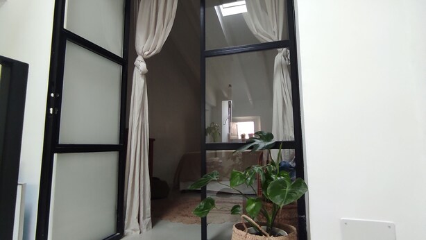 A room with a sliding glass door leading to a balcony, a potted plant on the balcony, and a small table with a chair. - Bright and airy townhouse (Soller)