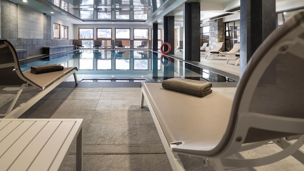 Un área de piscina interior moderna con sillones de descanso y una pared de vidrio.