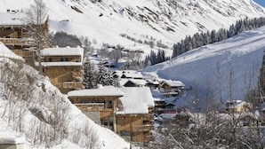 Un pueblo cubierto de nieve en la montaña con edificios de madera, pistas de esquí y un cielo despejado.