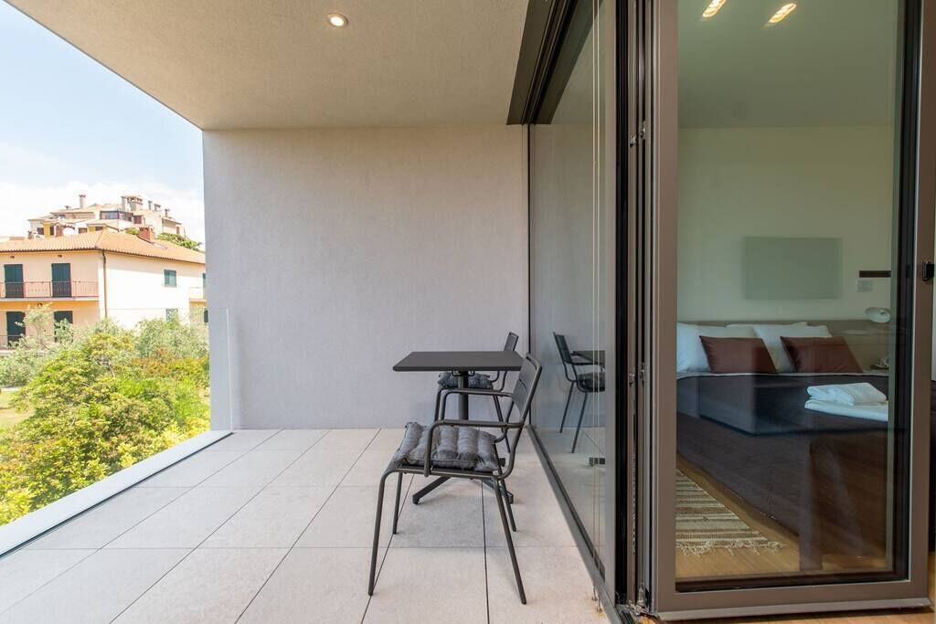 A balcony with a table and chairs, a glass door leading to a bedroom with a bed and pillows.
