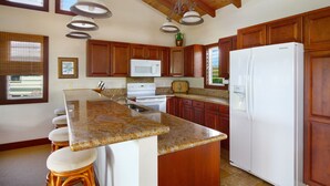 A kitchen with granite countertops, wooden cabinets, a white refrigerator, a microwave, and a stove.