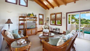 A spacious living room with wicker furniture, a glass coffee table, and a television on a wooden cabinet.
