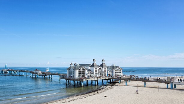 A coastal pier with a large building, a beach, and the sea.
