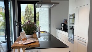 A modern kitchen with a central island, built-in appliances, and a view through the glass door.