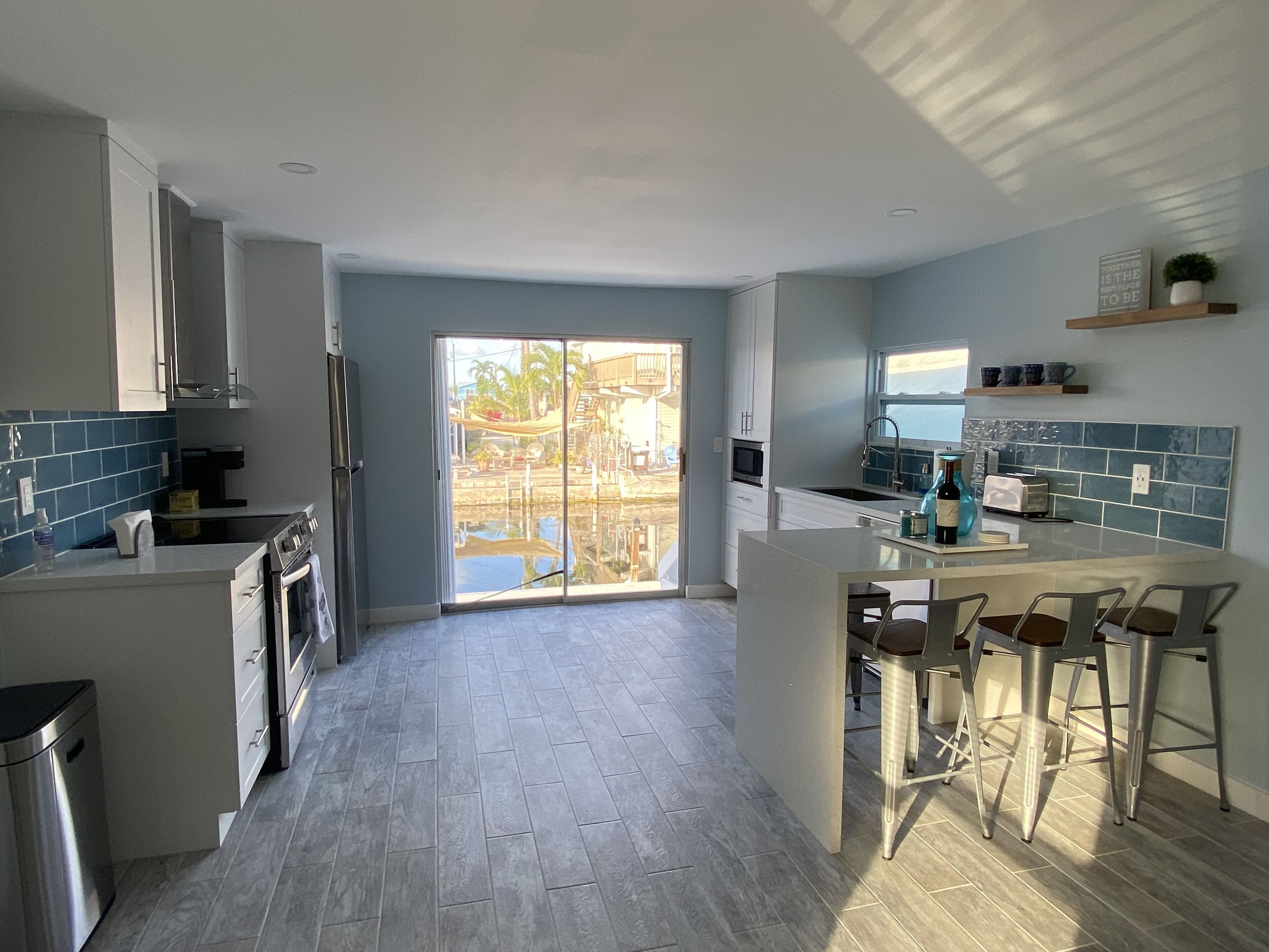 A modern kitchen with a central island, bar stools, and a view of a pool through the glass doors.