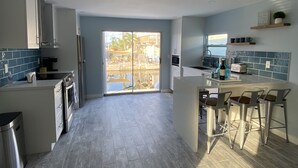 Een moderne keuken met een centraal eiland, een paar barkrukken en uitzicht op een zwembad door de glazen deuren.
