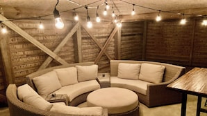 A cozy corner with a curved wicker sofa, a round ottoman, and a small table. - E-SEA-LIVIN' Oceanside Coastal Cottage in Corolla, 4 min walk to the beach! (Corolla)