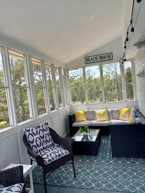 A sunroom with a sofa, chairs, and a sign reading 'BEACH HOUSE'. - E-SEA-LIVIN' Oceanside Coastal Cottage in Corolla, 4 min walk to the beach! (Corolla)