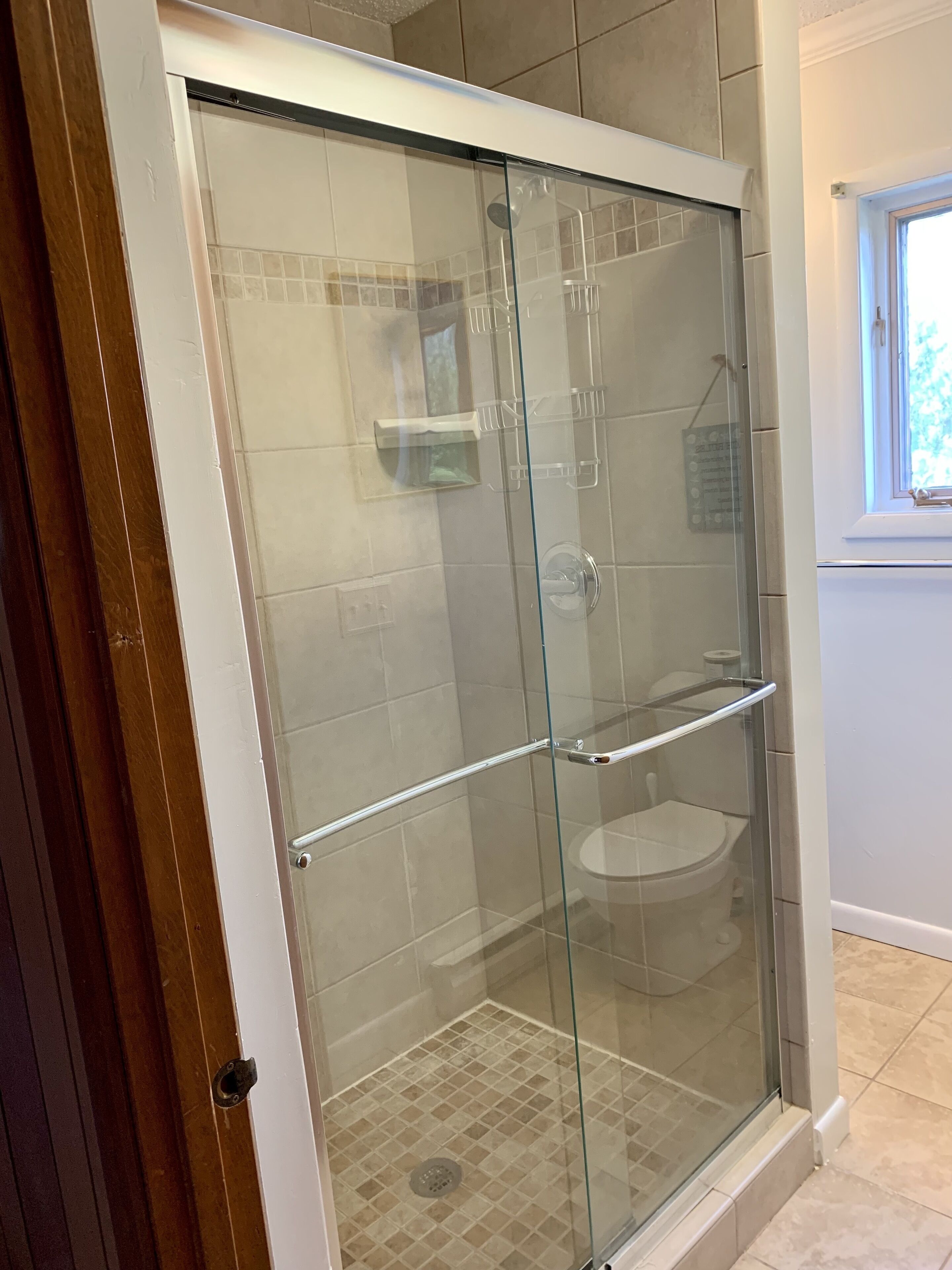 A glass-enclosed shower stall with a tiled floor and a toilet visible in the background.