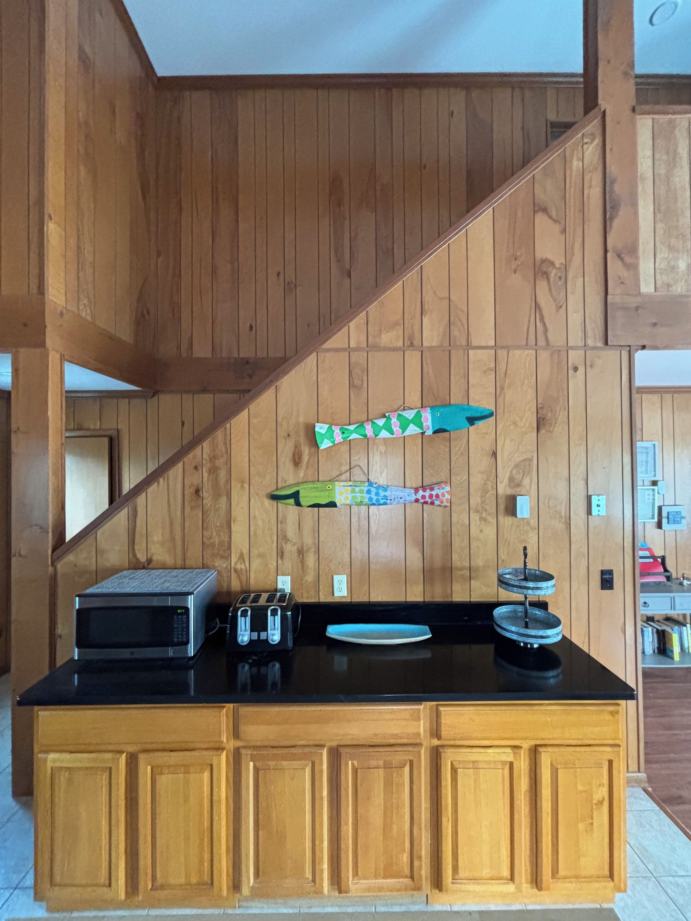 A kitchen with wooden paneling, a microwave, toaster, and a decorative fish on the wall.