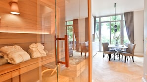 Ein modernes Hotelzimmer mit Glastrennwand, Holzvertäfelung, einem Essbereich mit Tisch und Stühlen und Blick ins Freie.