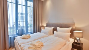 Ein Hotelzimmer mit einem großen Bett, zwei Nachttischen, einer Lampe und Blick ins Freie durch ein Fenster.