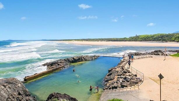 A coastal swimming area with clear water, rocky edges, and a sandy beach.