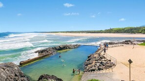 A coastal swimming area with clear water, rocky edges, and a sandy beach.