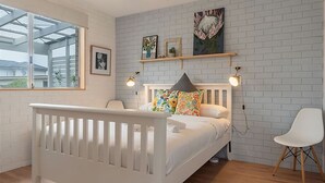 A modern bedroom with a white bed, colorful pillows, a white chair, and a brick-patterned wall.