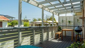 A covered outdoor deck with a wooden table and chairs, a hanging light fixture, and a view of surrounding buildings.