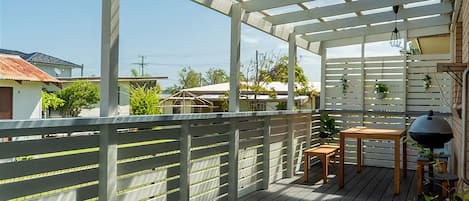 Una terraza techada al aire libre con una mesa y sillas de madera, un colgante de luz y vistas de edificios circundantes.