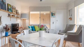 A modern living room with a white table, chairs, a TV, and a potted plant.