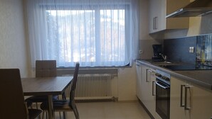 Una cucina compatta con un tavolo e sedie, una finestra con tende leggere e elettrodomestici moderni.