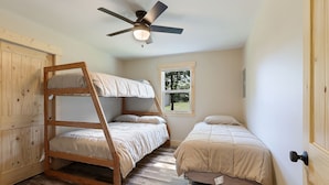 Una habitación con literas, una cama individual, un ventilador de techo, una ventana y paredes de madera.