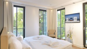 Une chambre d’hôtel moderne dotée d’un grand lit, d’un coin salon et d’un balcon offrant une vue sur la mer.