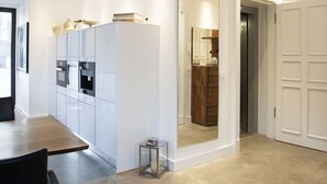 Une cuisine moderne avec des meubles blancs, un coin repas doté d’une table en bois, et un couloir menant à un placard en bois.