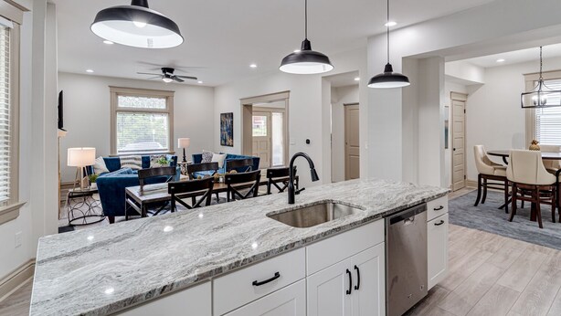 A modern kitchen with a marble countertop, black pendant lights, and a dining area with blue chairs and a white table. - ROOMY, COMFY, and CONVENIENT Historical Home (Cincinnati)