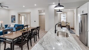 A modern kitchen with a marble countertop, stainless steel appliances, and a dining area with a blue sofa and wooden chairs. - ROOMY, COMFY, and CONVENIENT Historical Home (Cincinnati)