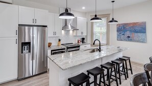 A modern kitchen with white cabinets, stainless steel appliances, a marble countertop, and black bar stools. - ROOMY, COMFY, and CONVENIENT Historical Home (Cincinnati)