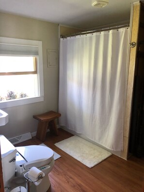 A bathroom with a toilet, a small wooden stool, a shower curtain, and a window. - Quiet property on lake Oneida (Brewerton)