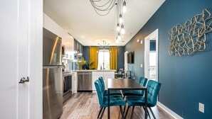 A modern kitchen with stainless steel appliances, a dining area with teal chairs, and a blue accent wall. - Cozy Modern Home in Downtown Atlanta (Atlanta)