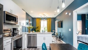 A compact kitchen with modern appliances, a dining area with a wooden table, and a view of the outdoors through a window with yellow curtains. - Cozy Modern Home in Downtown Atlanta (Atlanta)