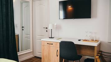 A hotel room with a wooden desk, a chair, a TV mounted on the wall, and a door with a mirror.