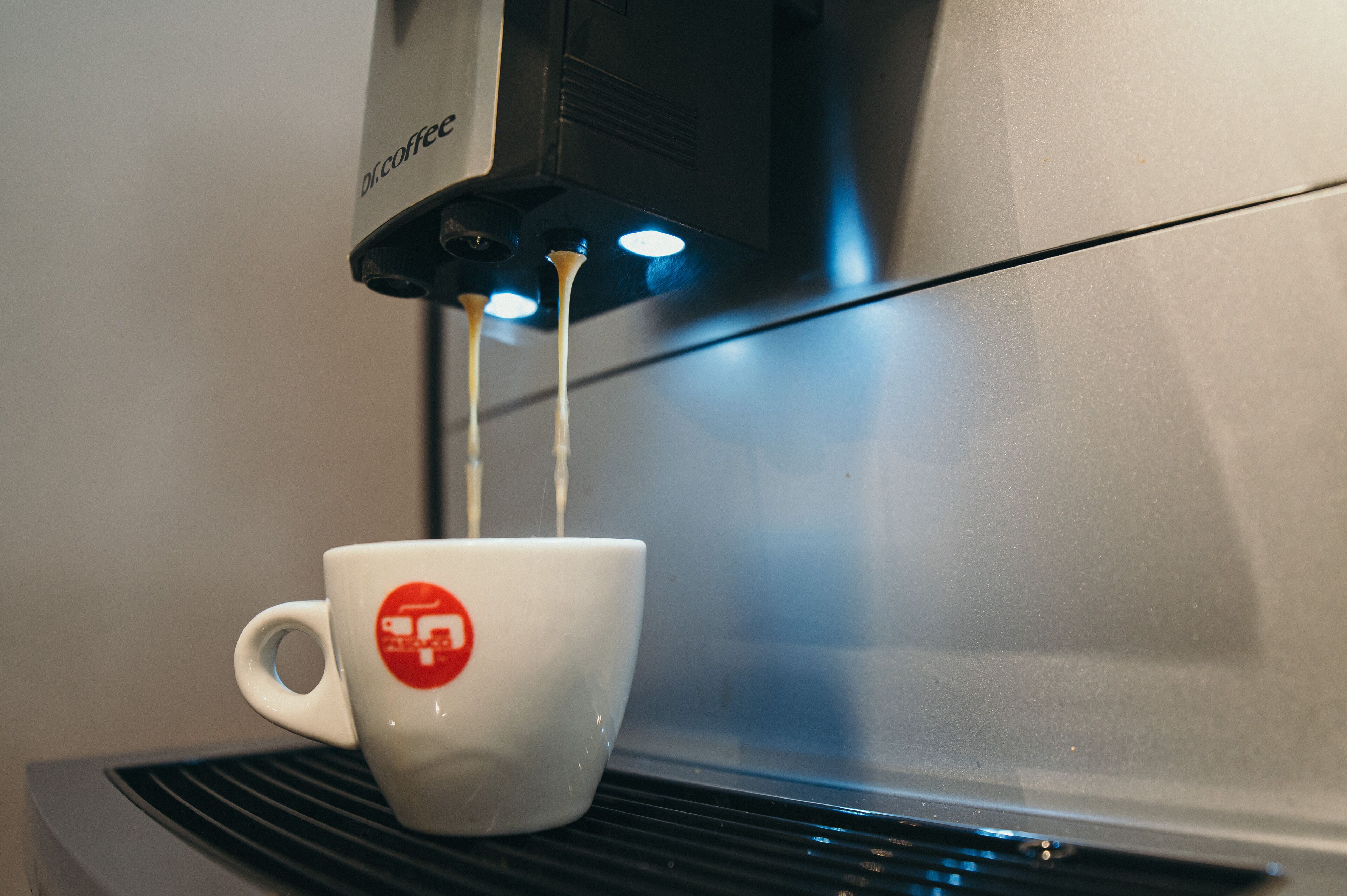 Una cafetera sirviendo café en una taza blanca con un logotipo rojo.