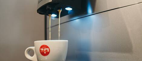 Una cafetera sirviendo café en una taza blanca con un logotipo rojo.