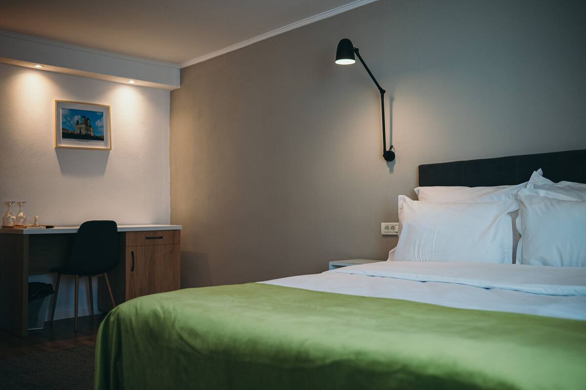 Ein Hotelzimmer mit Bett, Schreibtisch, Stuhl und einer Wandlampe.