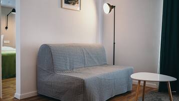 Una habitación con un sofá gris, una mesita blanca, una lámpara de pie y un cuadro en la pared.