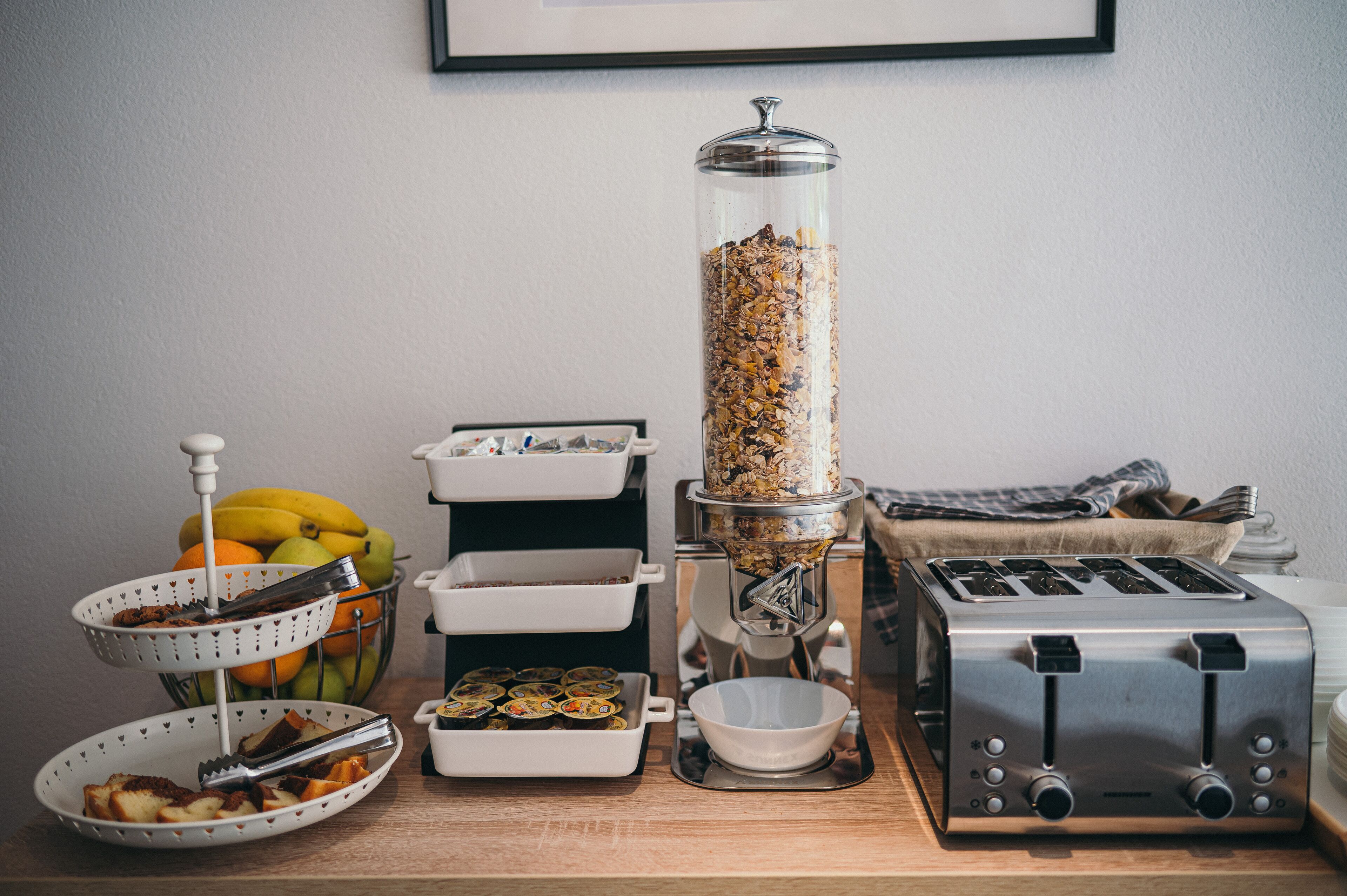 Een aanrecht met een koffiezetapparaat, een broodrooster en verschillende etenswaren, waaronder een fruitschaal en een muffinvorm.