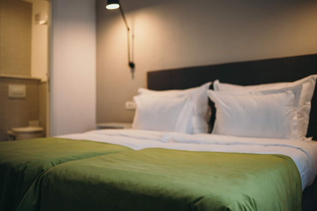 Ein Hotelzimmer mit Bett, grüner Bettdecke, weißen Kissen und einem Nachttisch mit Lampe.