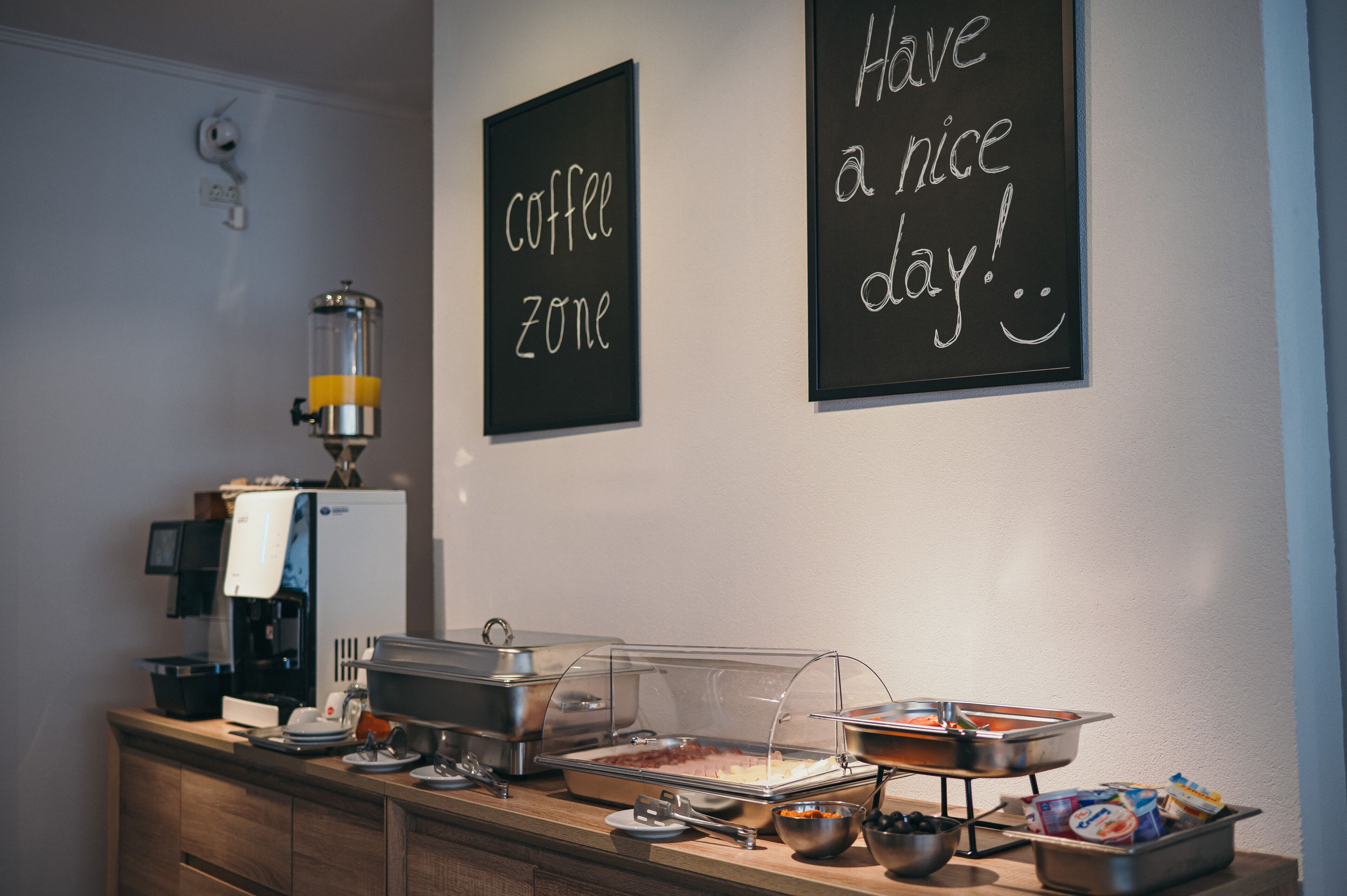 A buffet setup with a coffee machine, a coffee zone sign, and a sign saying "Have a nice day!".