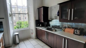 A kitchen with dark cabinets, a stainless steel sink, and a window overlooking a building. - Cornwall Street [297] is a Spacious and charming apartment close to Usher Hall (Edinburgh)